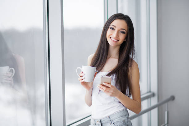istock Woman in shorts drinking coffee at home window 1146349080