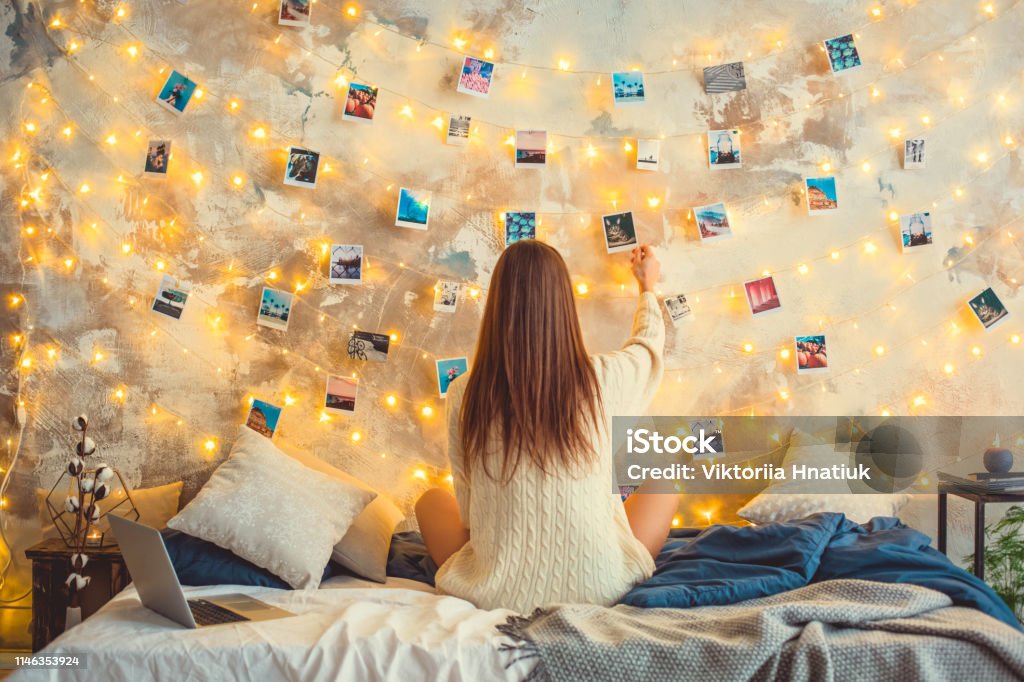 Young woman weekend at home decorated bedroom nostalgia Young woman creative weekend at home sitting looking at the photos on lighted wall memories nostalgia Teenager Stock Photo