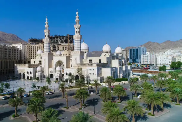 a white mosque in mecca surrounded by buildings and mountains