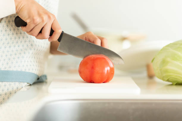 femme au foyer coupant une tomate avec un couteau de cuisine - stereotypical homemaker photos et images de collection