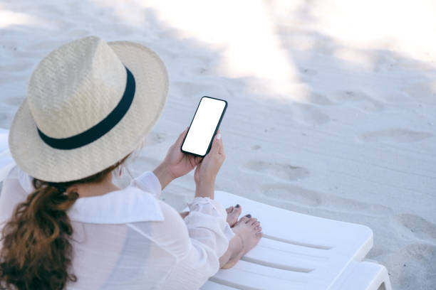 istock a woman holding white mobile phone with blank desktop screen while sitting on beach chair 1146370583