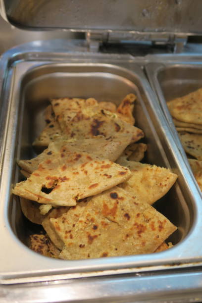 Stock photo of North Indian breakfast dish, self service buffet offering slices of aloo parathas, traditional Indian recipe. Savoury bread stuffed with garam masala potatoes and onions. imagen de la india del norte plato de desayuno buffet con autoservicio rebanadas de aloo parathas receta (aalu parotha), pan salado relleno con patatas de garam masala, hotel restaurante casero aloo paratha plato, yogur raita cuajada, pepinillo picante, de