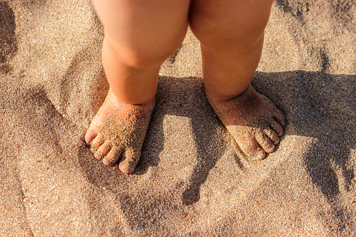 Baby feet walking on sand beach in the summer. Close up.