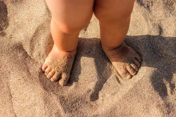 Photo of Baby feet walking on sand beach in the summer.
