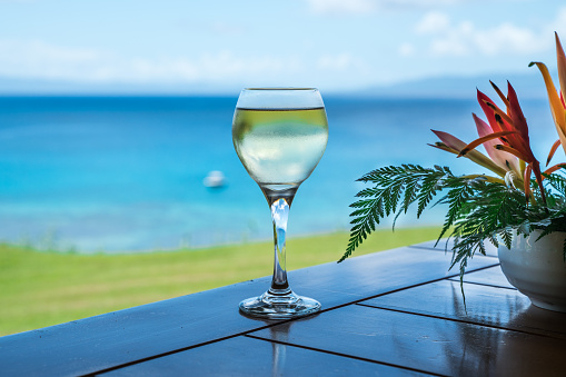 White wine by the ocean on a table with a nicely decorated flower vase next to it