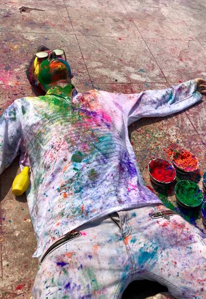 imagem do turista inglês feliz do homem que comemora a luta da pintura de holi sorrindo em nova deli, india, festival de holi das cores que encontram-se para baixo sunbathing coberto no gulal da cor do pó da pintura da face soou, parte superior branca de - human face india new delhi traditional culture - fotografias e filmes do acervo