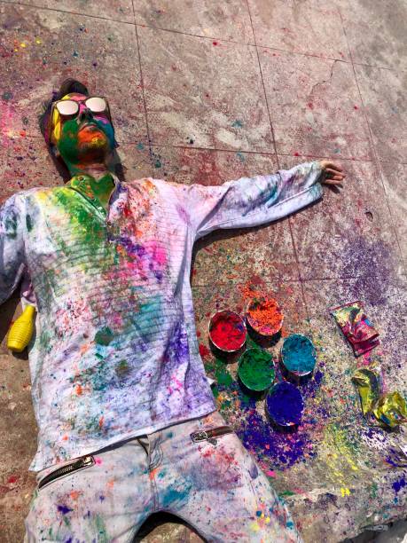 imagem do turista inglês feliz do homem que comemora a luta da pintura de holi sorrindo em nova deli, india, festival de holi das cores que encontram-se para baixo sunbathing coberto no gulal da cor do pó da pintura da face soou, parte superior branca de - human face india new delhi traditional culture - fotografias e filmes do acervo