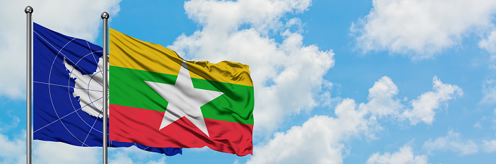 Antarctica and Myanmar flag waving in the wind against white cloudy blue sky together. Diplomacy concept, international relations.