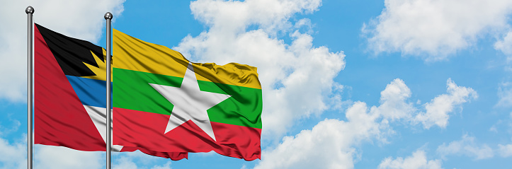 Antigua and Barbuda with Myanmar flag waving in the wind against white cloudy blue sky together. Diplomacy concept, international relations.