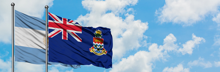 Argentina and Cayman Islands flag waving in the wind against white cloudy blue sky together. Diplomacy concept, international relations.