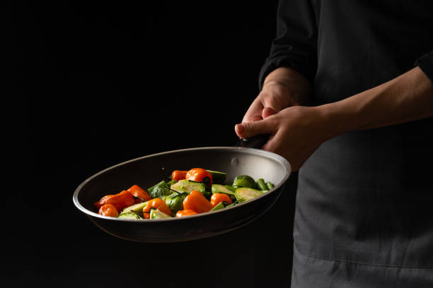 istock Chef preparing vegetables in a pan, Asian cuisine, on a black background for design, recipe book, menu, restaurant or hotel sign, cooking, gastronomy 1146416491