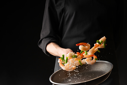 Seafood, Professional cook prepares shrimps with sprigg beans. Frost in the air, Cooking seafood, healthy vegetarian food and food on a dark background. Horizontal view. Eastern kitchen, banner