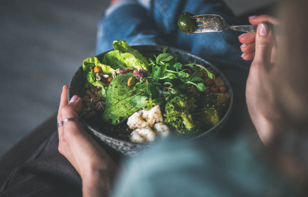 Healthy vegan championship game in hands of woman at home Healthy dinner or lunch at home. Vegan championship game or Buddha bowl with hummus, vegetable, fresh salad, beans, couscous and avocado in female hands foxys_forest_manufacture stock pictures, royalty-free photos & images