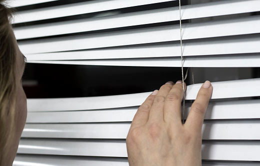 woman peeping through the blinds on the street.