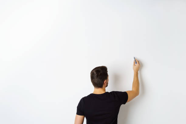 Man writing on white wall Rear view of man writing on white wall with copy space writing on chalk board stock pictures, royalty-free photos & images