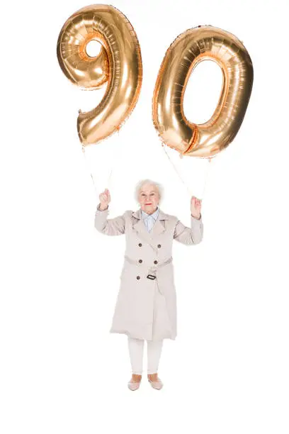 happy senior woman holding 90 golden balloons isolated on white