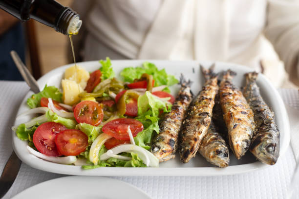 sardinas a la brasa con ensalada y aceite de oliva sobre plato blanco - prepared fish fish grilled close up fotografías e imágenes de stock