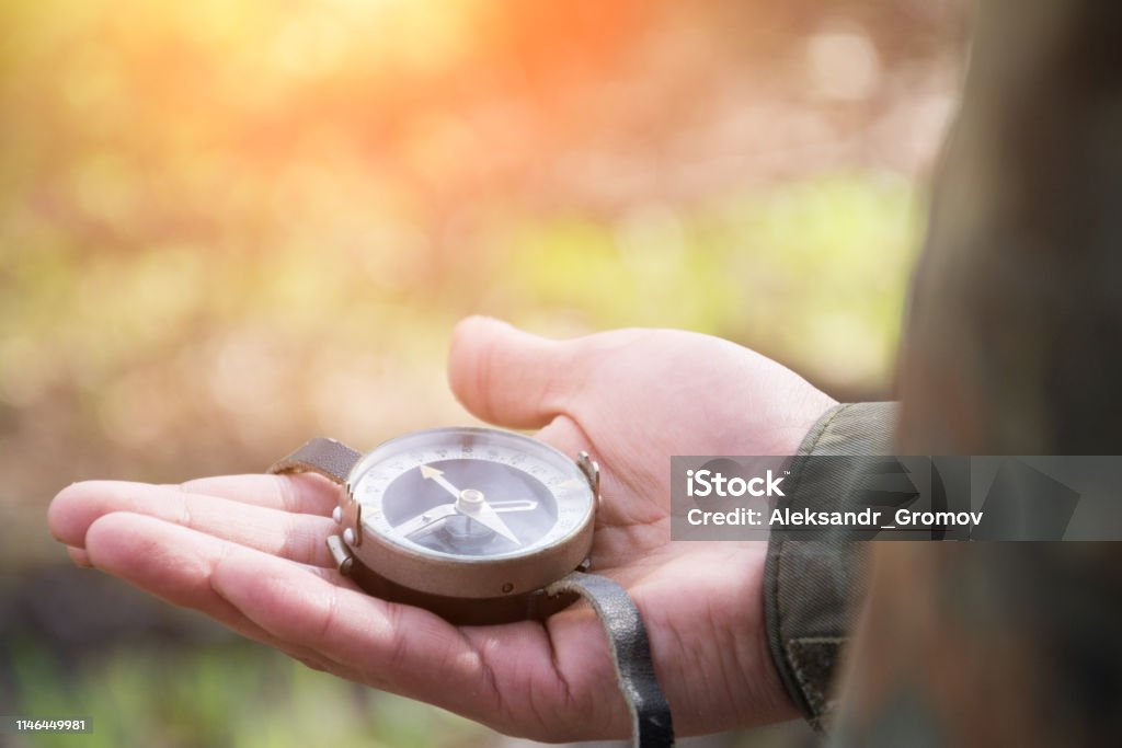 male hand holds a magnetic compass male hand holds a magnetic compass, forest hike Navigational Compass Stock Photo