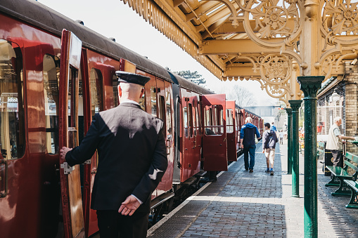 Sheringham, UK - April 21, 2019: Conductor in uniform closing a door of retro Poppy Line steam train at Sheringham station. Sheringham is an English seaside town within the county of Norfolk, UK.