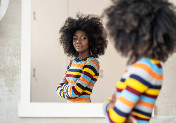 afro woman looking at her reflection in the mirror - mirror imagens e fotografias de stock