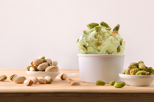 Pistachios ice cream cup decorated with pistachio chunks on a plate on a wooden table. Horizontal composition. Front view.