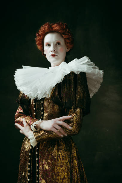 Medieval young woman as a duchess Too serious. Medieval redhead young woman in golden vintage clothing as a duchess standing crossing hands on dark green background. Concept of comparison of eras, modernity and renaissance. duchess photos stock pictures, royalty-free photos & images