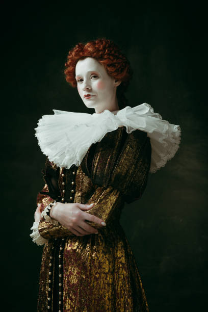 Medieval young woman as a duchess I am the one. Medieval redhead young woman in golden vintage clothing as a duchess standing crossing hands on dark green background. Concept of comparison of eras, modernity and renaissance. duchess photos stock pictures, royalty-free photos & images