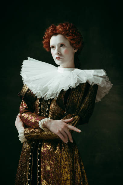 Medieval young woman as a duchess Capricious nature. Medieval redhead young woman in golden vintage clothing as a duchess standing crossing hands on dark green background. Concept of comparison of eras, modernity and renaissance. duchess photos stock pictures, royalty-free photos & images
