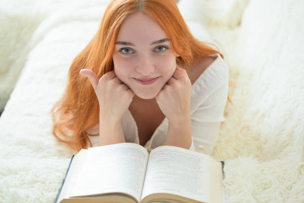 a beautiful young woman is reading a book on the couch in her room