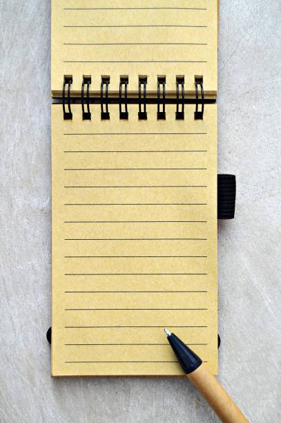 istock A single lined blank yellow beige page of a spiral bound vertical notepad and brown and black color pen placed on top, over a wooden look beige color grungy vintage vertical background. 1146466801