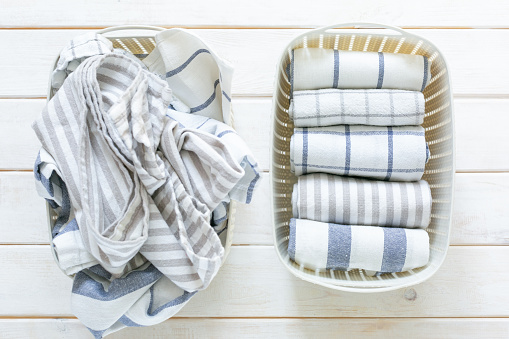 Marie Kondo tidying concept - folded kitchen linens in white basket, top view