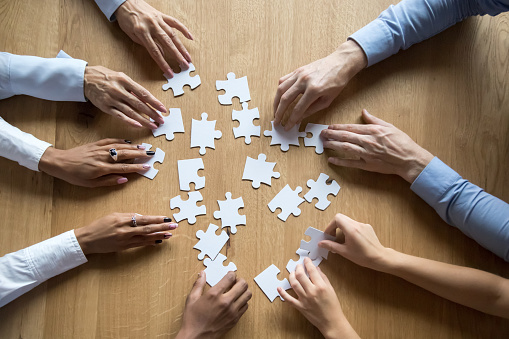 Diverse business team people hands assemble puzzle together connect pieces at desk, employees collaborate find common solution engaged help contribute in effective teamwork concept top close up view