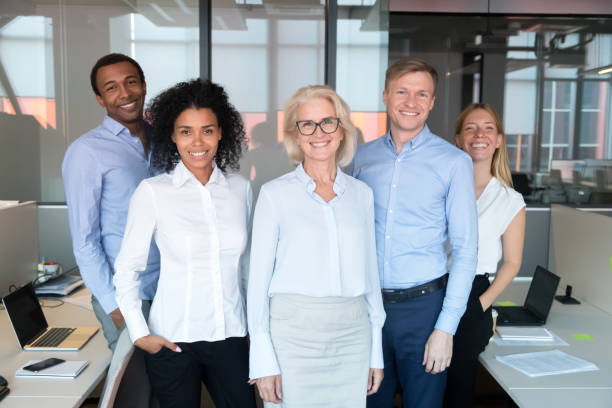 happy professional team with old female business leader posing together - reduction looking at camera finance business imagens e fotografias de stock