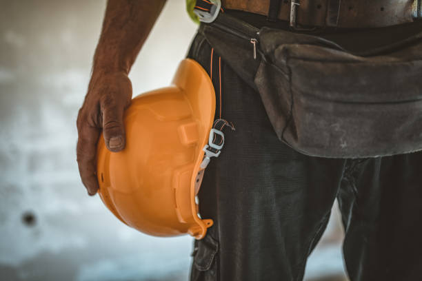 Close-up View of Construction Worker at the Interior of Building Site, who is Standing with his Yellow Helmet, Working Tools and Equipment.