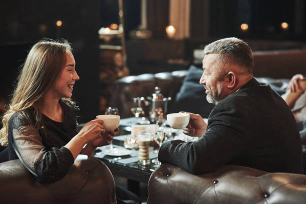 istock Good mood. Conversation between young and older generation. Family friends have nice evening near the fireplace in luxury modern restaurant 1146469588