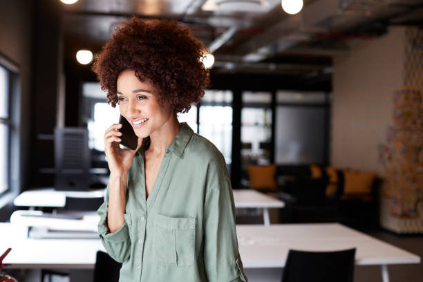 istock Millennial black female creative standing in an open plan office using smartphone, close up 1146471145