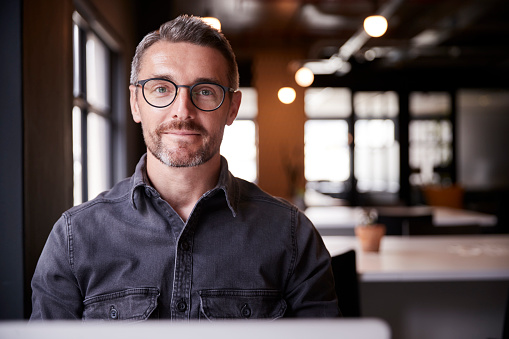 Creativo masculino blanco de mediana edad sentado en una oficina sonriendo a la cámara, la cabeza y los hombros, de cerca photo