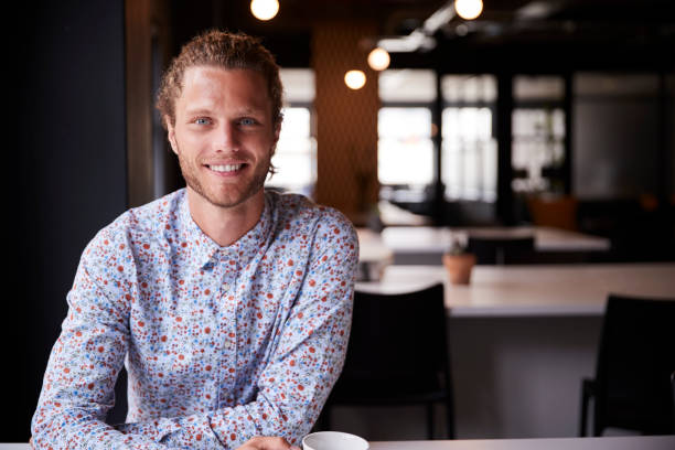 istock Millennial white male creative sitting at a desk in an open plan office smiling to camera, close up 1146472736