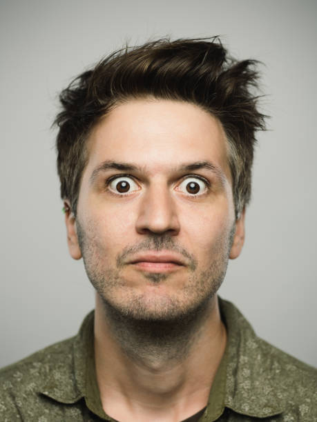 Real caucasian man with surprised expression looking at camera Close up portrait of young adult man with sursprised expression looking at camera against gray white background. Vertical shot of caucasian real people shocked in studio with brown hair and modern spiky haircut. Photography from a DSLR camera. Sharp focus on eyes. staring stock pictures, royalty-free photos & images
