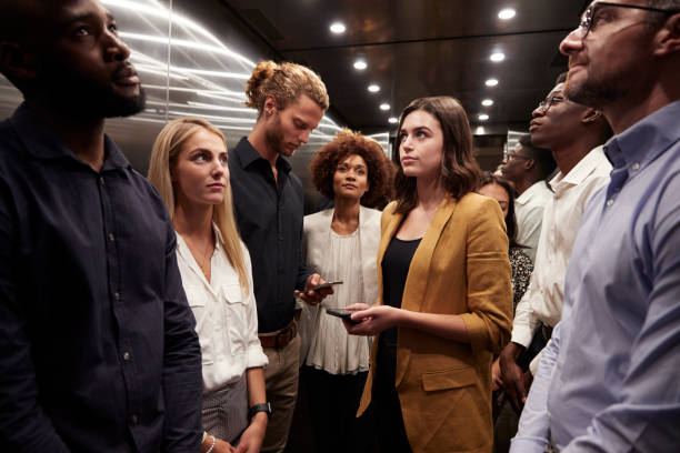 work colleagues stand waiting together in an elevator at their office - busy imagens e fotografias de stock