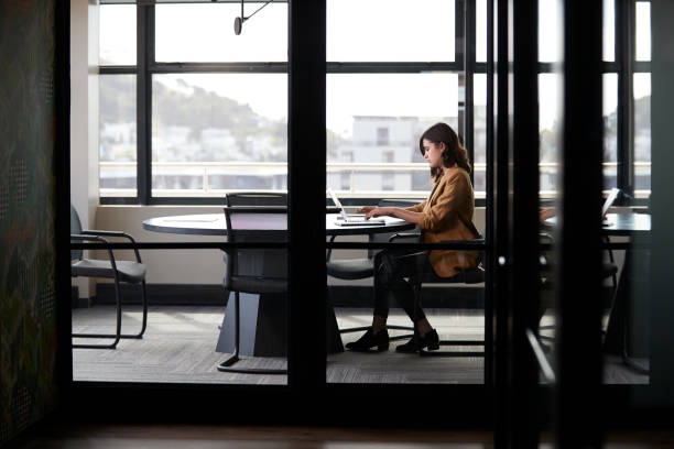 Millennial white creative businesswoman working alone in a meeting room, seen through glass wall Millennial white creative businesswoman working alone in a meeting room, seen through glass wall rolled up sleeves stock pictures, royalty-free photos & images