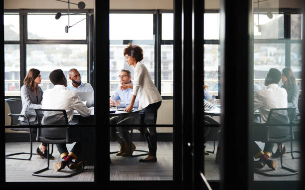 a mulher de negócios preta millennial está endereçando colegas em uma reunião, vista através da parede de vidro - door office business women - fotografias e filmes do acervo