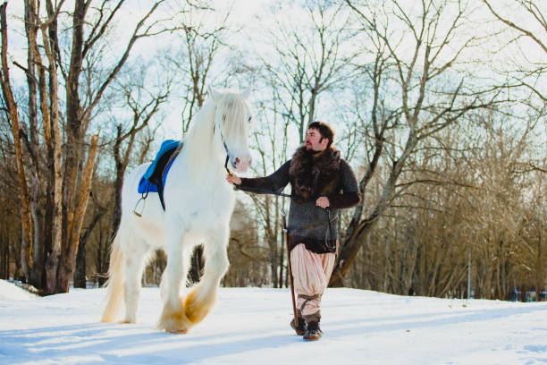 Man in suit of ancient warrior walking with the big white horse stock photo