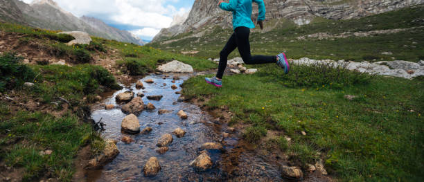 istock Woman trail runner jumping over small river on beautiful mountains 1146473585