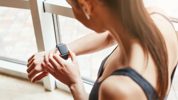 quelle heure est-il? recadrée photo de jeune femme en sportswear vérifiant le temps sur son bracelet de sport tout en restant devant la fenêtre à la salle de gym - musical instrument people music young adult photos et images de collection