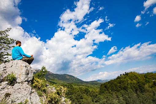 Young Adult Man Meditating on a Rock in Nature.