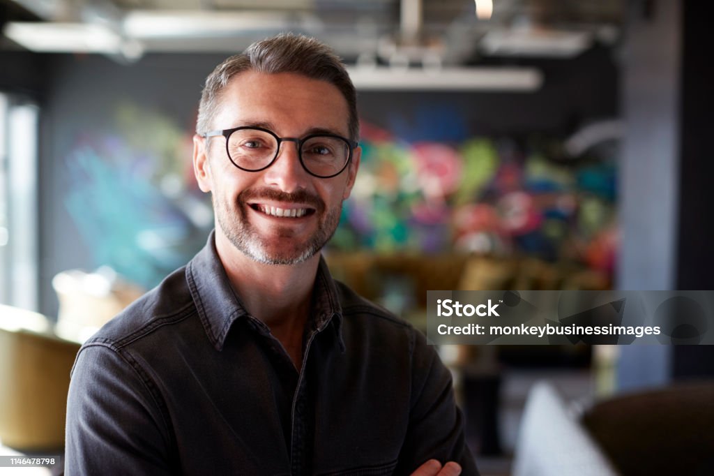 Middle aged white male creative in casual office lounge area looks to camera smiling, close up Men Stock Photo