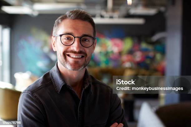 Middle Aged White Male Creative In Casual Office Lounge Area Looks To Camera Smiling Close Up Stock Photo - Download Image Now