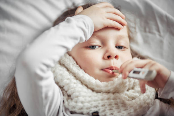 a sick little girl lying in bed with a thermometer stock photo