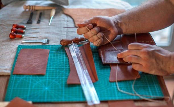 istock Working process of the leather belt in the leather workshop. Man holding crafting tool and working. Tanner in old tannery. Wooden table background. Close up man arm 1146484985